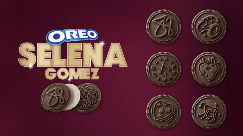 
Uma imagem promocional para os biscoitos Oreo de edição limitada da Selena Gomez. À esquerda, o logotipo da Oreo aparece acima de "Selena Gomez" em letras douradas. Abaixo do nome, há dois biscoitos Oreo. Um é um Oreo reverso com o recheio de chocolate e os biscoitos de baunilha, e o outro é um Oreo tradicional. À direita, há seis biscoitos Oreo de chocolate com desenhos em relevo. Os designs incluem: as iniciais "SG", uma borboleta, uma nota musical, um coração, e outras ilustrações. O fundo é um gradiente de tons de roxo e marrom.