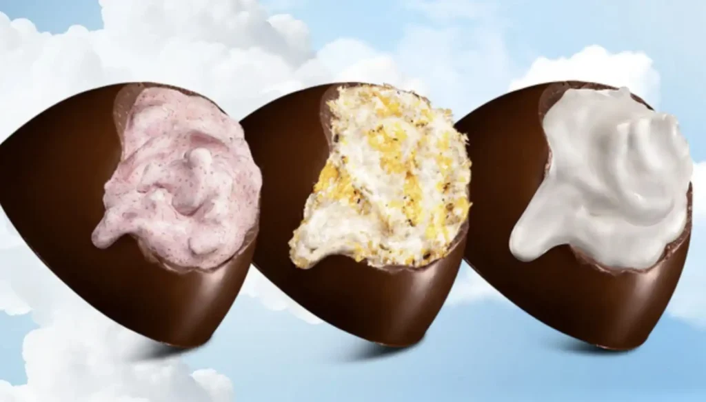 Três bombons de chocolate dispostos lado a lado. O bombom da esquerda tem um recheio cremoso rosa-claro. O bombom do meio tem um recheio branco granulado com pedaços amarelados. O bombom da direita tem um recheio cremoso branco puro.