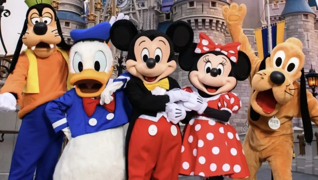 Cinco personagens da Disney em fantasias completas posando em frente ao Castelo da Cinderela. Da esquerda para a direita estão Pateta, Pato Donald, Mickey Mouse, Minnie Mouse e Pluto.