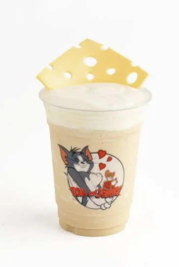 Copo com bebida da WE COFFEE com adesivo de Tom e Jerry e um queijo de chocolate branco.