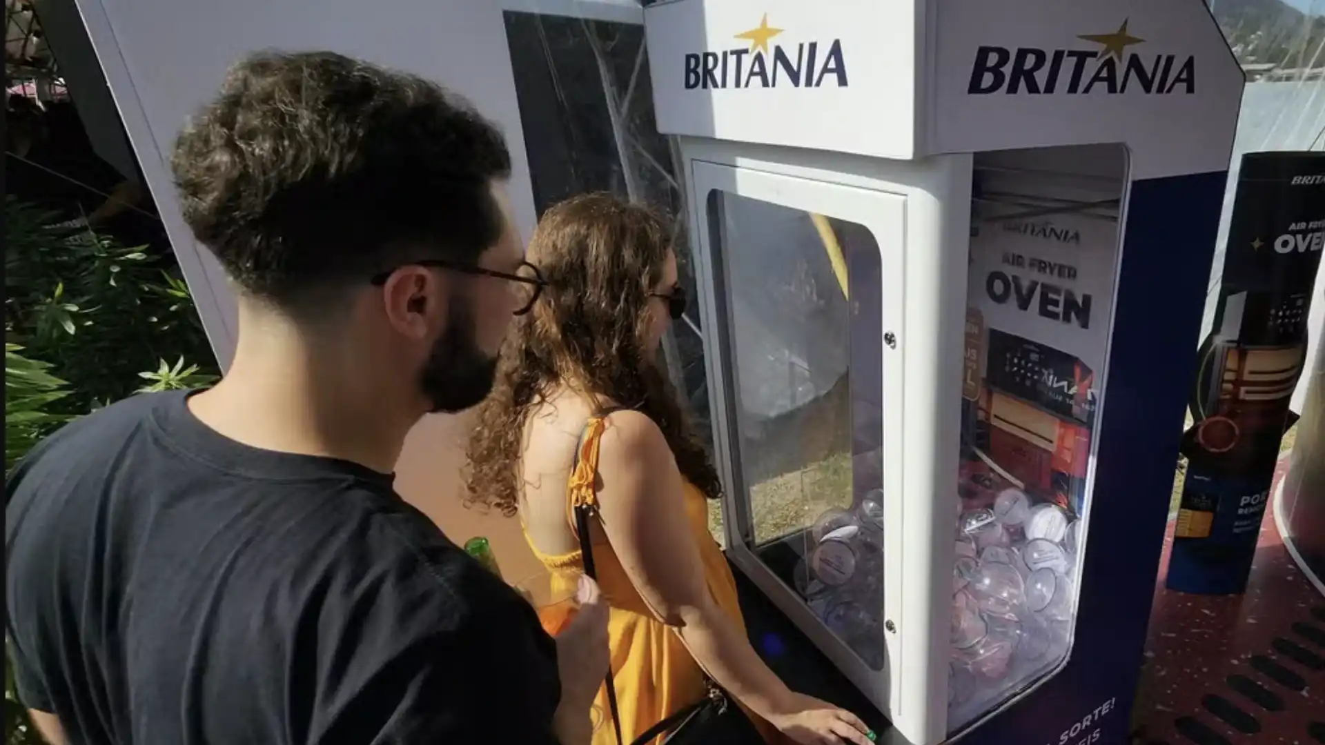 Um homem e uma mulher, vistos de lado, estão olhando para uma máquina de prêmios da marca Britania.