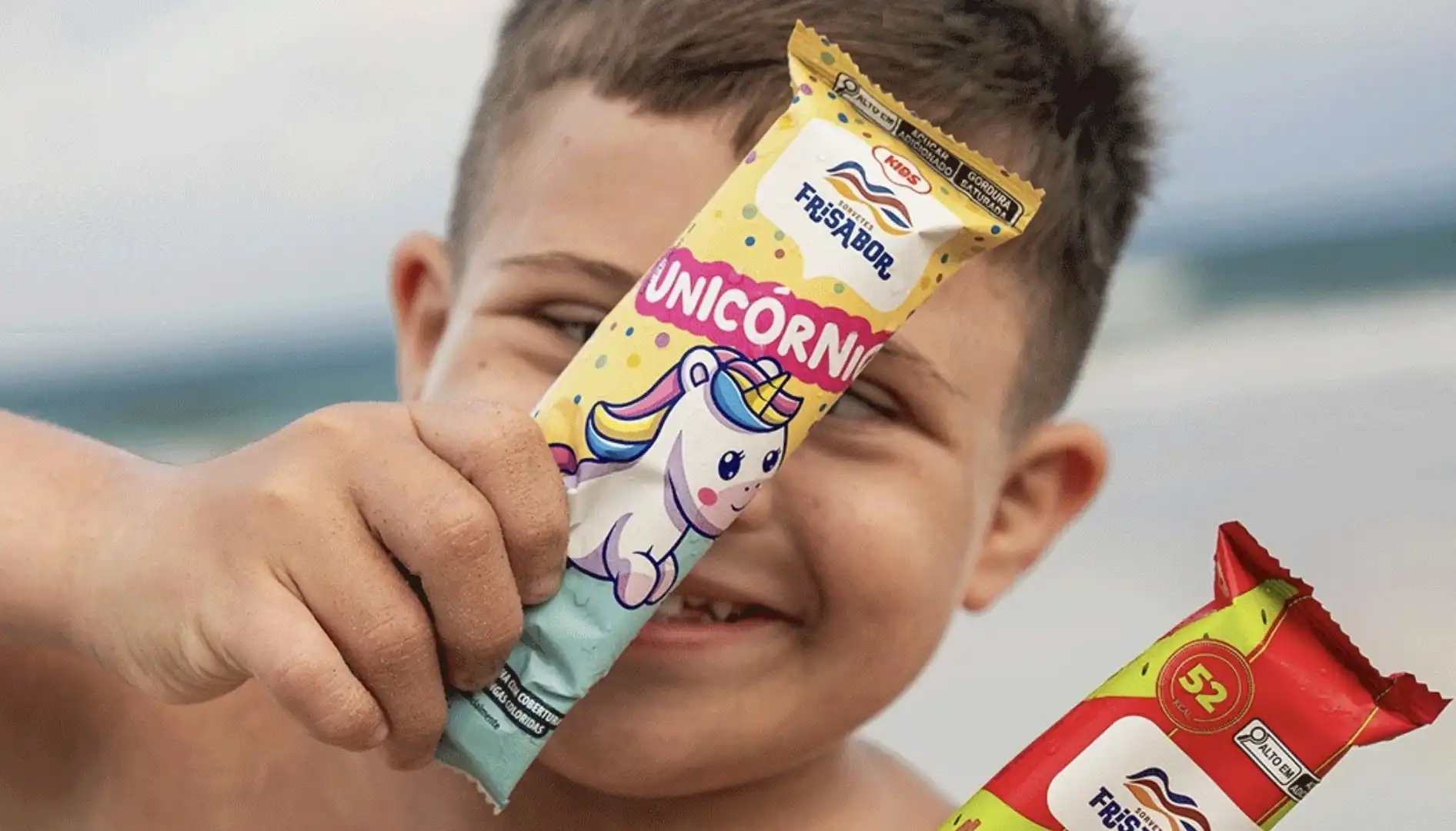Um menino sorridente segura um picolé Frisabor sabor unicórnio.