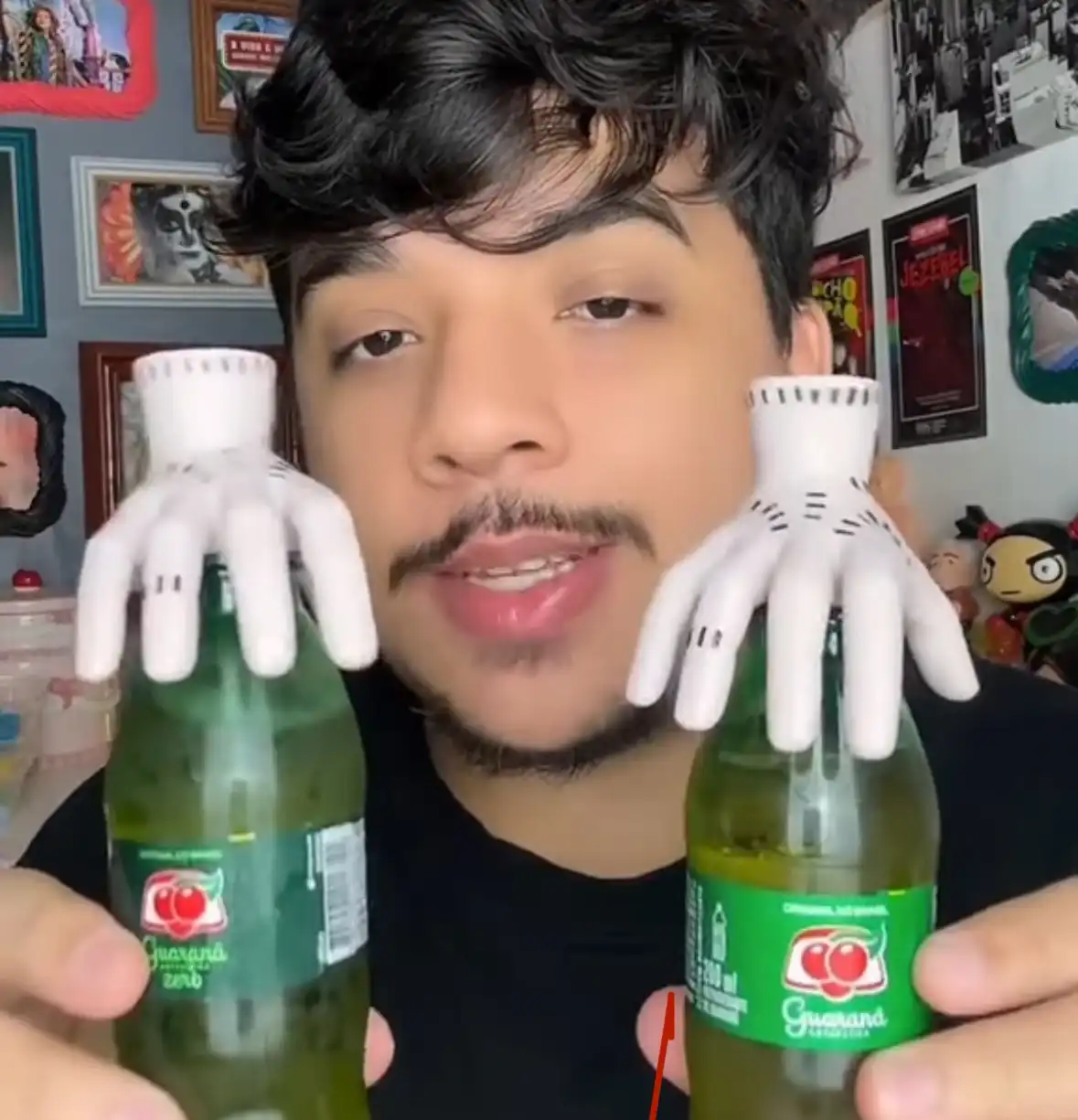 Homem com bigode e cavanhaque segurando duas garrafas de Guaraná Antarctica de 200ml, que têm pequenas mãos de monstro de Halloween em suas tampas.