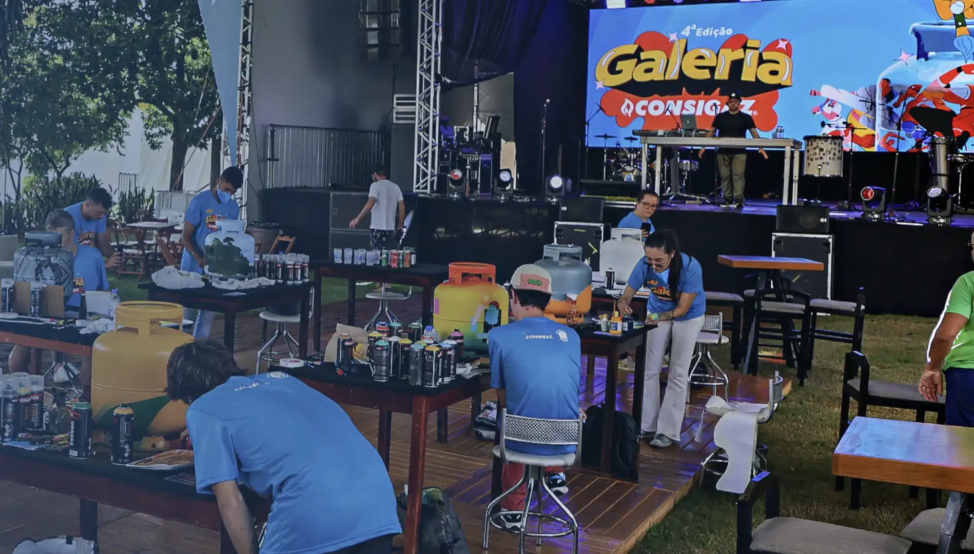o fundo, um palco com uma tela grande mostra a logo da "Galeria Consigaz".