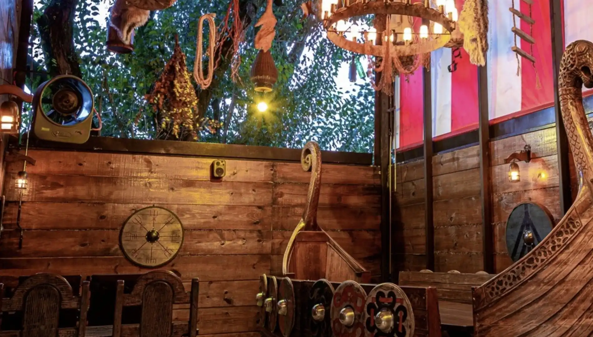 Interior de um restaurante temático viking com paredes de madeira, um lustre rústico, decoração com escudos e uma proa de navio viking.