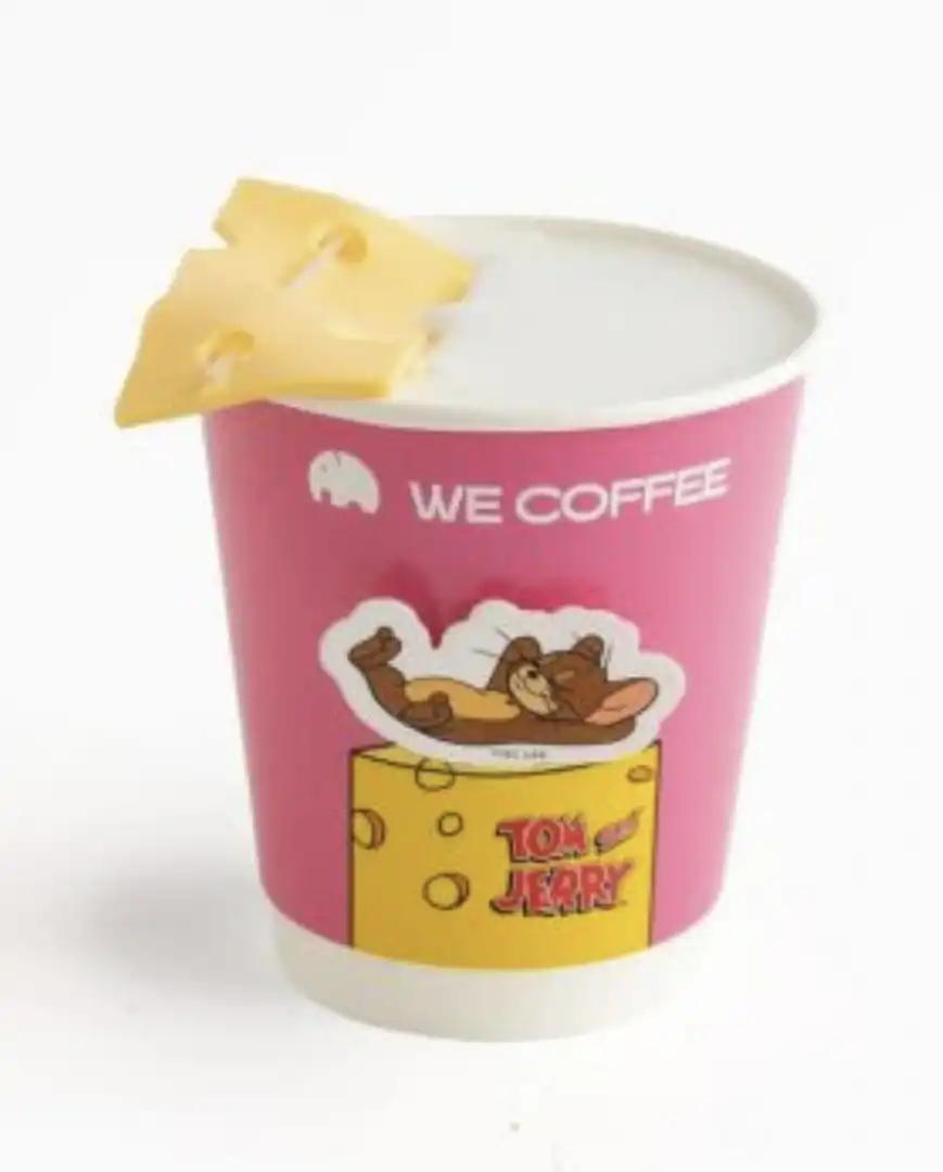 Copo de café da WE COFFEE com adesivo de Tom e Jerry e fatia de queijo.