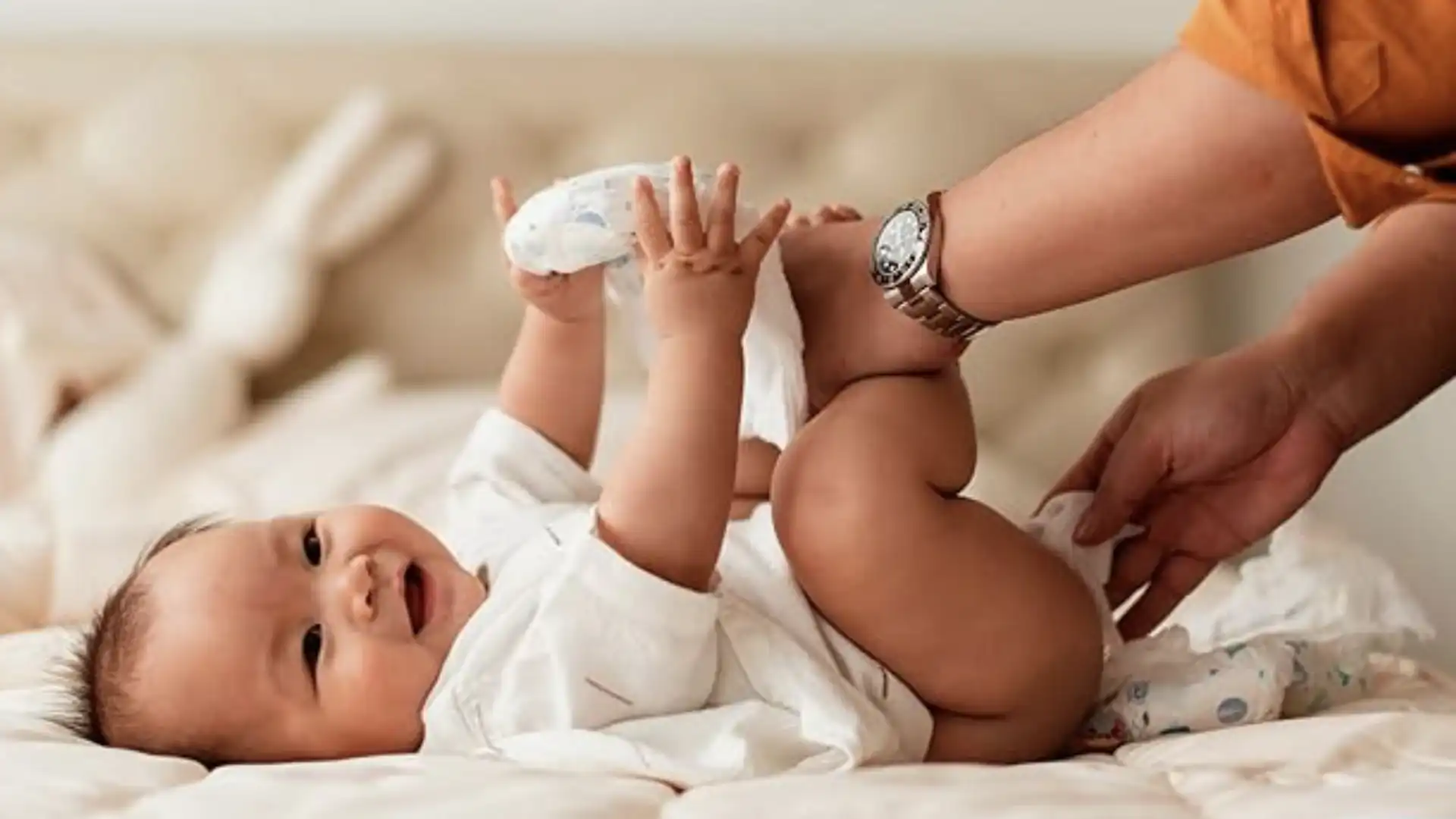 Mão de adulto segurando as pernas de um bebê para passar um lenço umedecido.