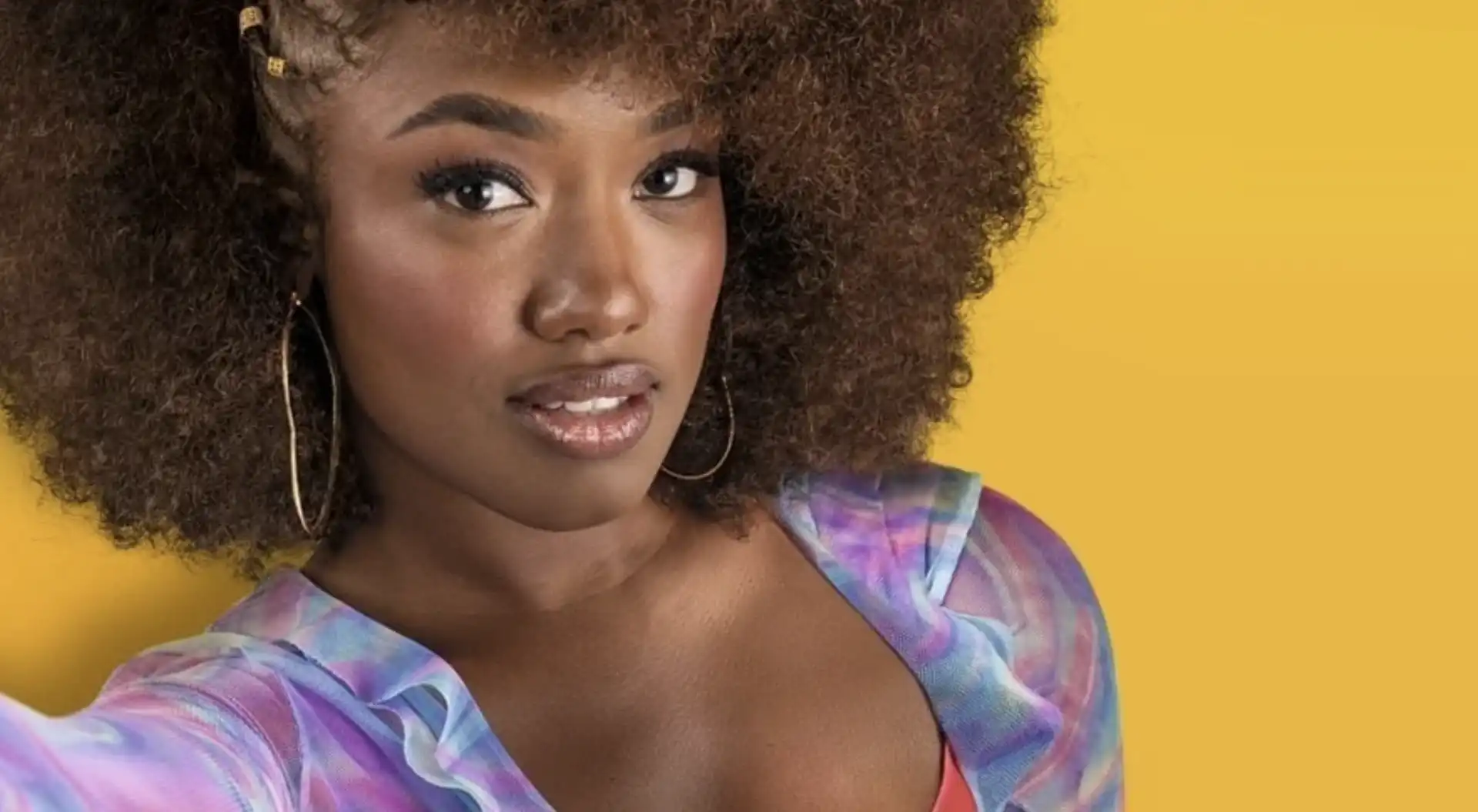 Retrato de uma mulher negra sorrindo, com cabelo encaracolado e brincos grandes