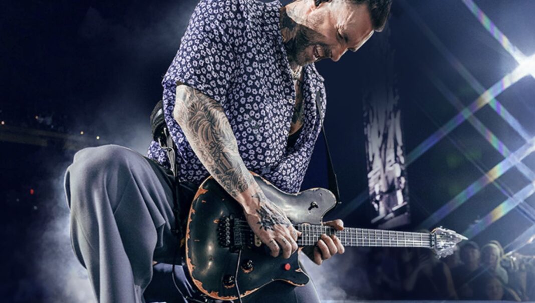 Adam Levine, vocalista do Maroon 5, tocando guitarra com intensidade em um show.