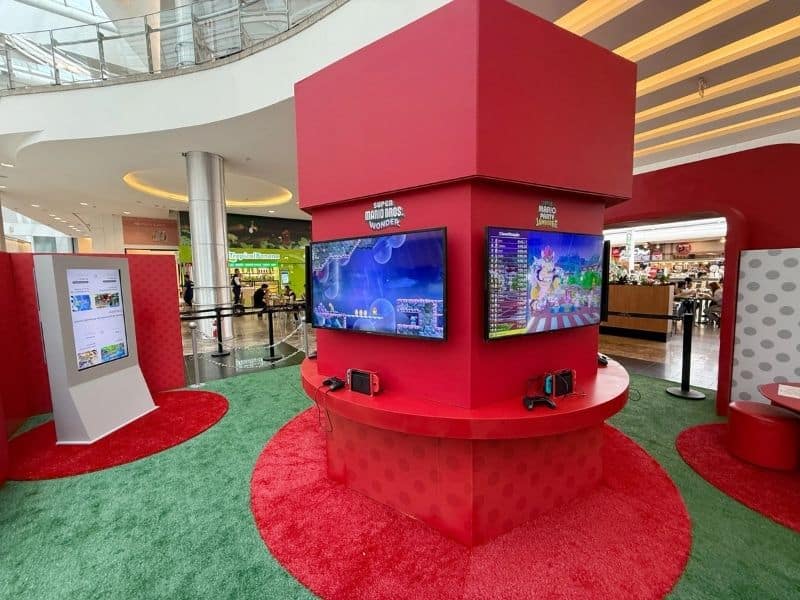Estação de jogos da Nintendo Switch em um shopping, com telas exibindo Super Mario Bros. Wonder e Mario Party Superstars.