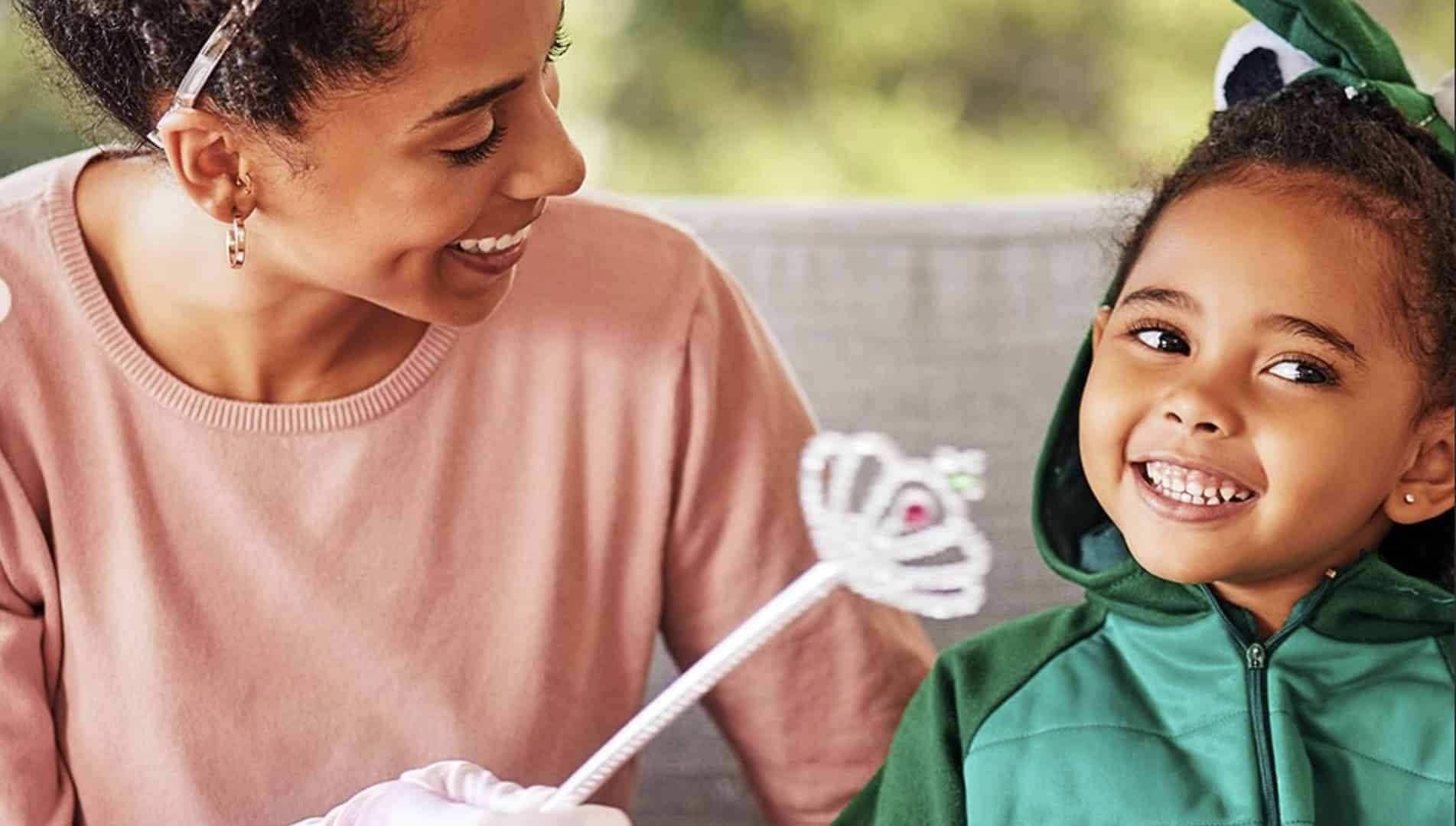 Mãe e filha fantasiada de dinossauro sorrindo com varinha de fada.