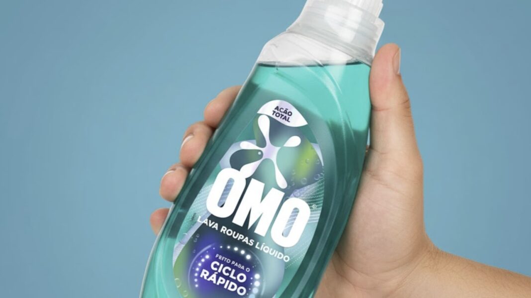 Uma mão segura um frasco de OMO Lava Roupas Líquido com o fundo azul.