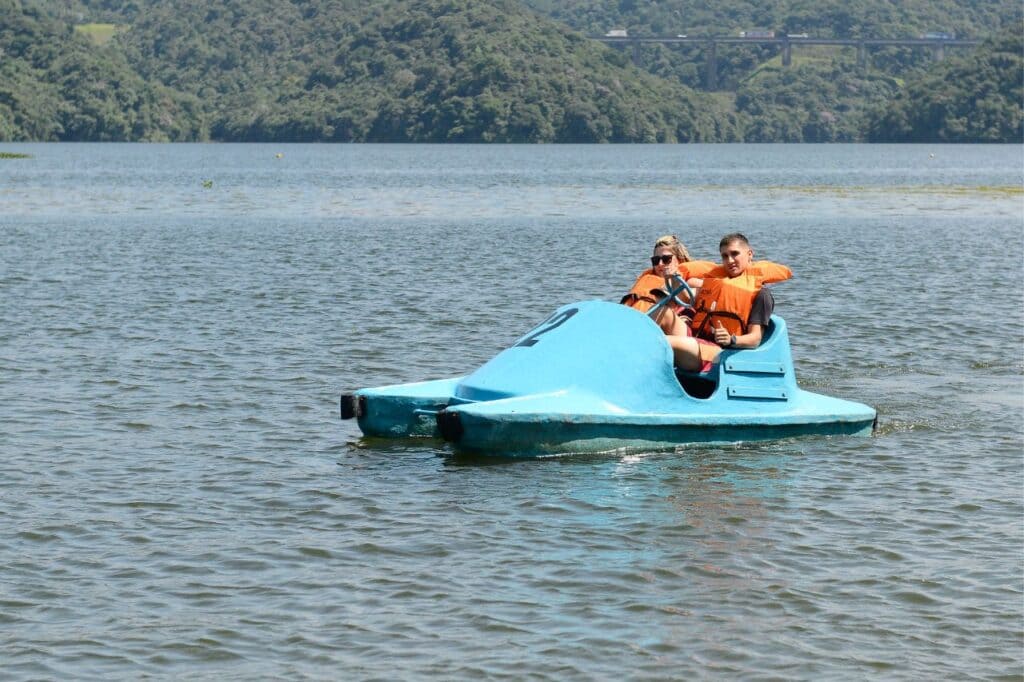 Casal em um pedalinho azul no lago do Parque Estoril, usando coletes salva-vidas.