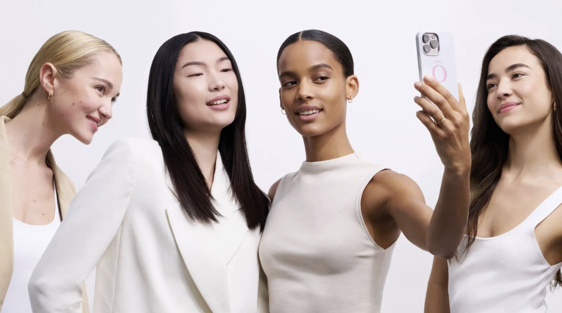 Quatro mulheres sorrindo, uma delas segurando um celular para tirar uma selfie.