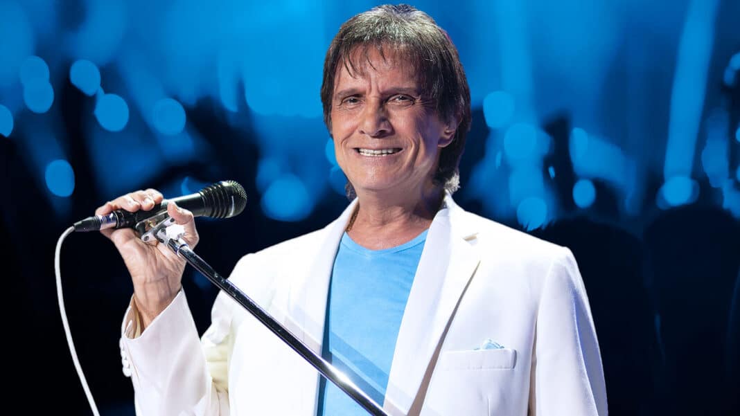 Retrato de Roberto Carlos, cantor brasileiro, sorrindo e segurando um microfone em um palco.