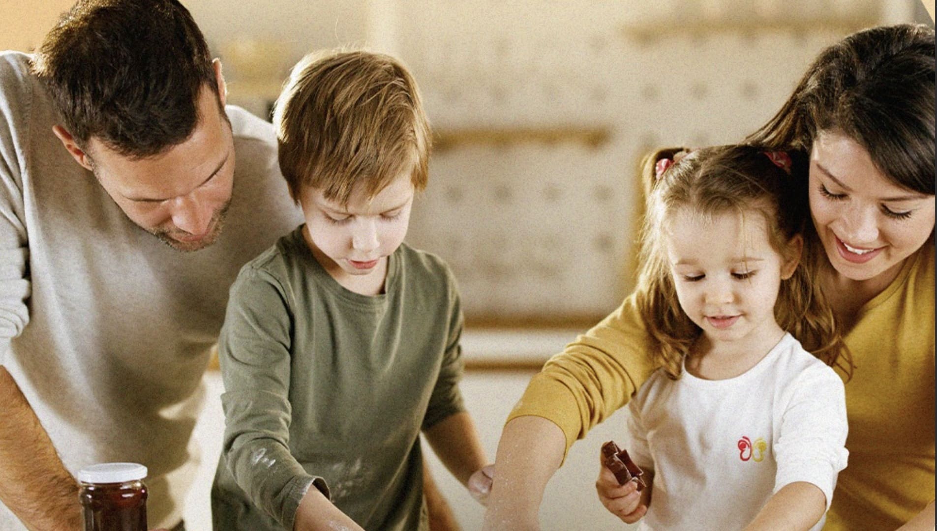Uma família (pai, mãe, um menino e uma menina) interagindo e cozinhando juntos em uma cozinha bem iluminada.