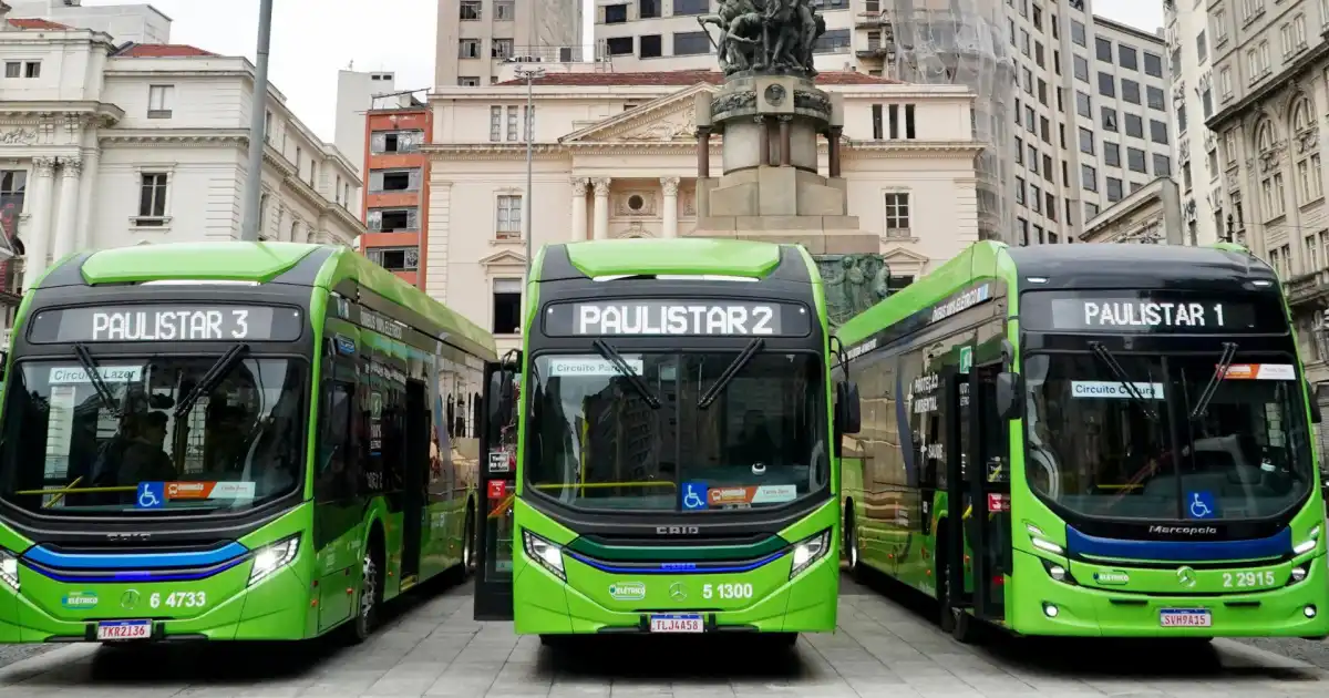 Três ônibus elétricos verdes da linha Paulistar estacionados lado a lado no centro de São Paulo, com edifícios históricos ao fundo.