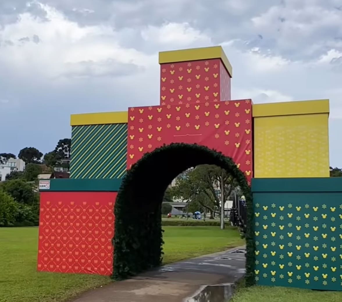 Grande estrutura em formato de portal feita de caixas de presente gigantes com temas da Disney, em um parque.Grande estrutura em formato de portal feita de caixas de presente gigantes com temas da Disney, em um parque.