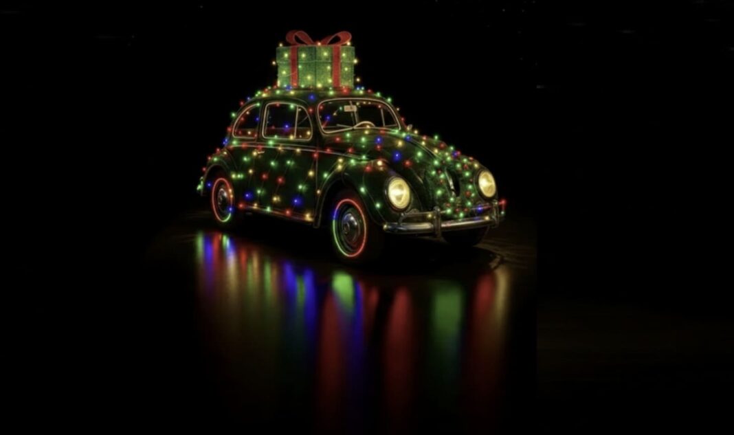 Fotografia de um Fusca clássico decorado com luzes de Natal coloridas e um grande presente verde no teto, iluminado contra um fundo preto com reflexos coloridos no chão.