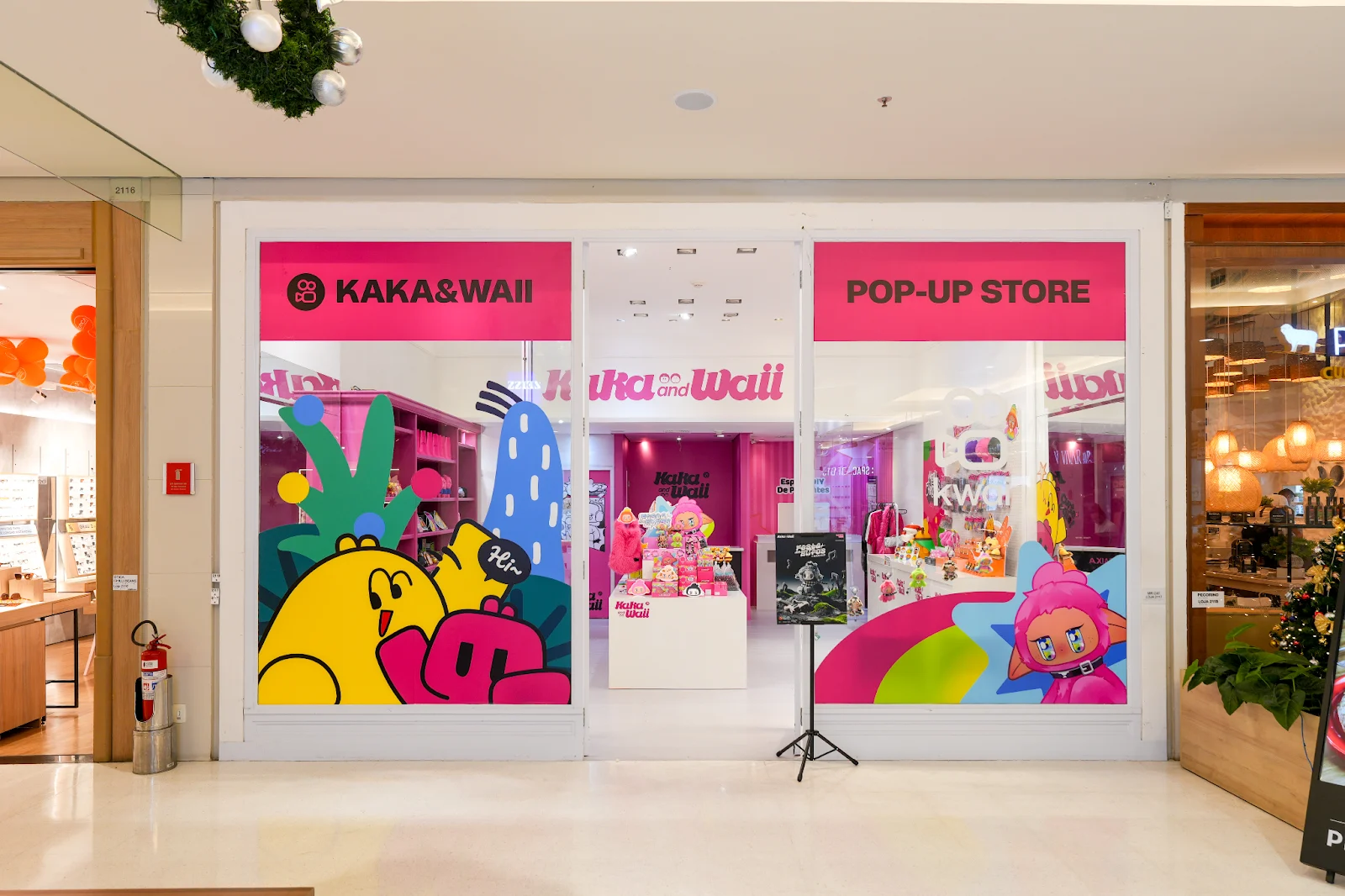 Fachada vibrante de uma Pop-Up Store do Kwai chamada "KAKA&WAII" em um shopping center, com decoração colorida e personagens de desenho animado.