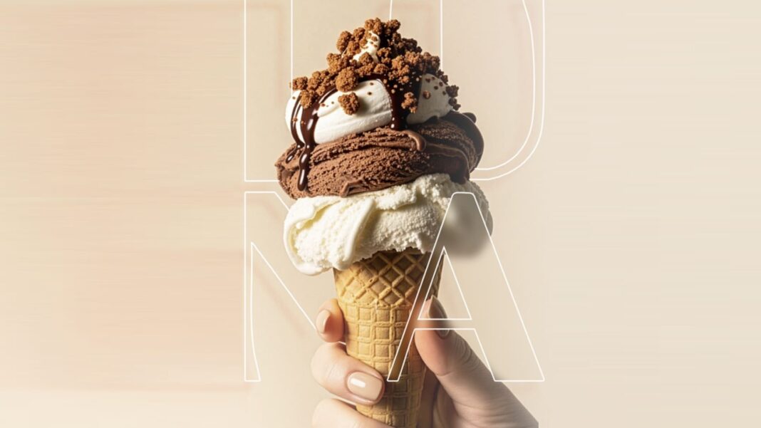 Close de uma mão segurando uma casquinha de gelato com três generosas camadas — creme na base, chocolate no meio e baunilha no topo — finalizada com calda de chocolate e pedaços de biscoito crocante.