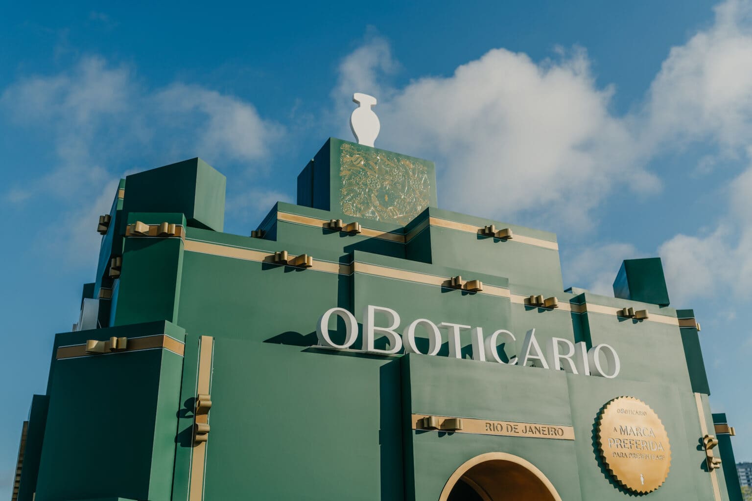 Estrutura verde monumental com a inscrição "OBOTICÁRIO" em letras brancas, sob um céu azul.