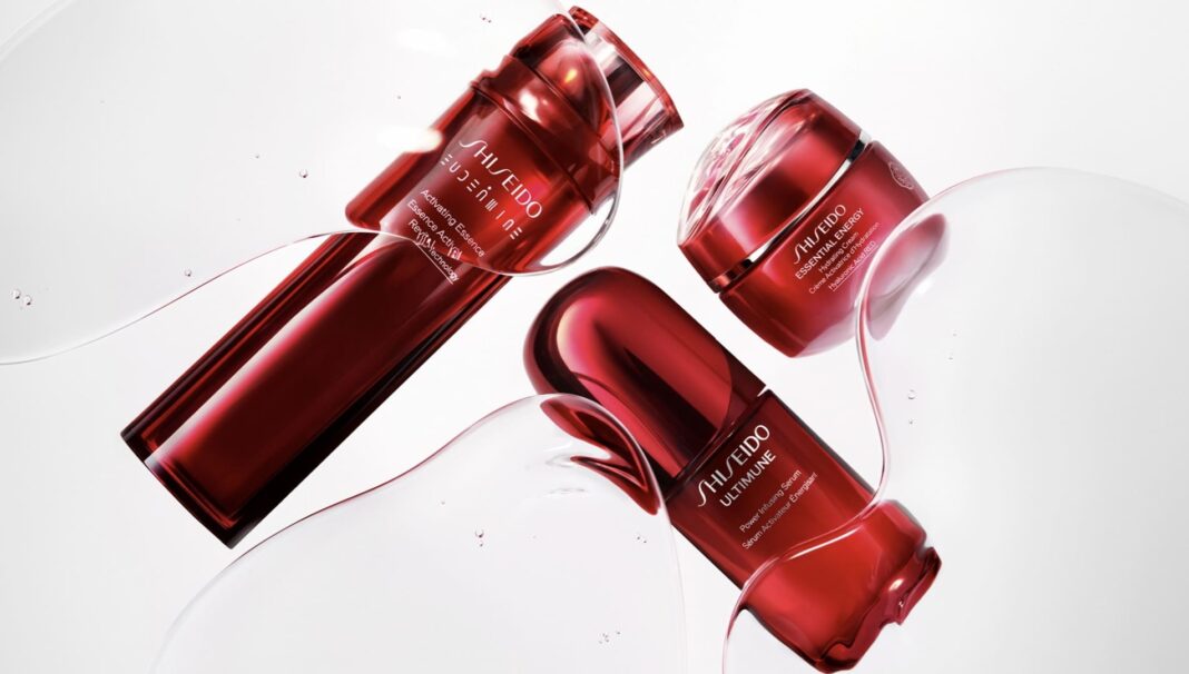 Três produtos de skincare Shiseido em embalagens vermelhas e elegantes (um creme e dois sérums/essências) flutuando em bolhas de líquido transparente.