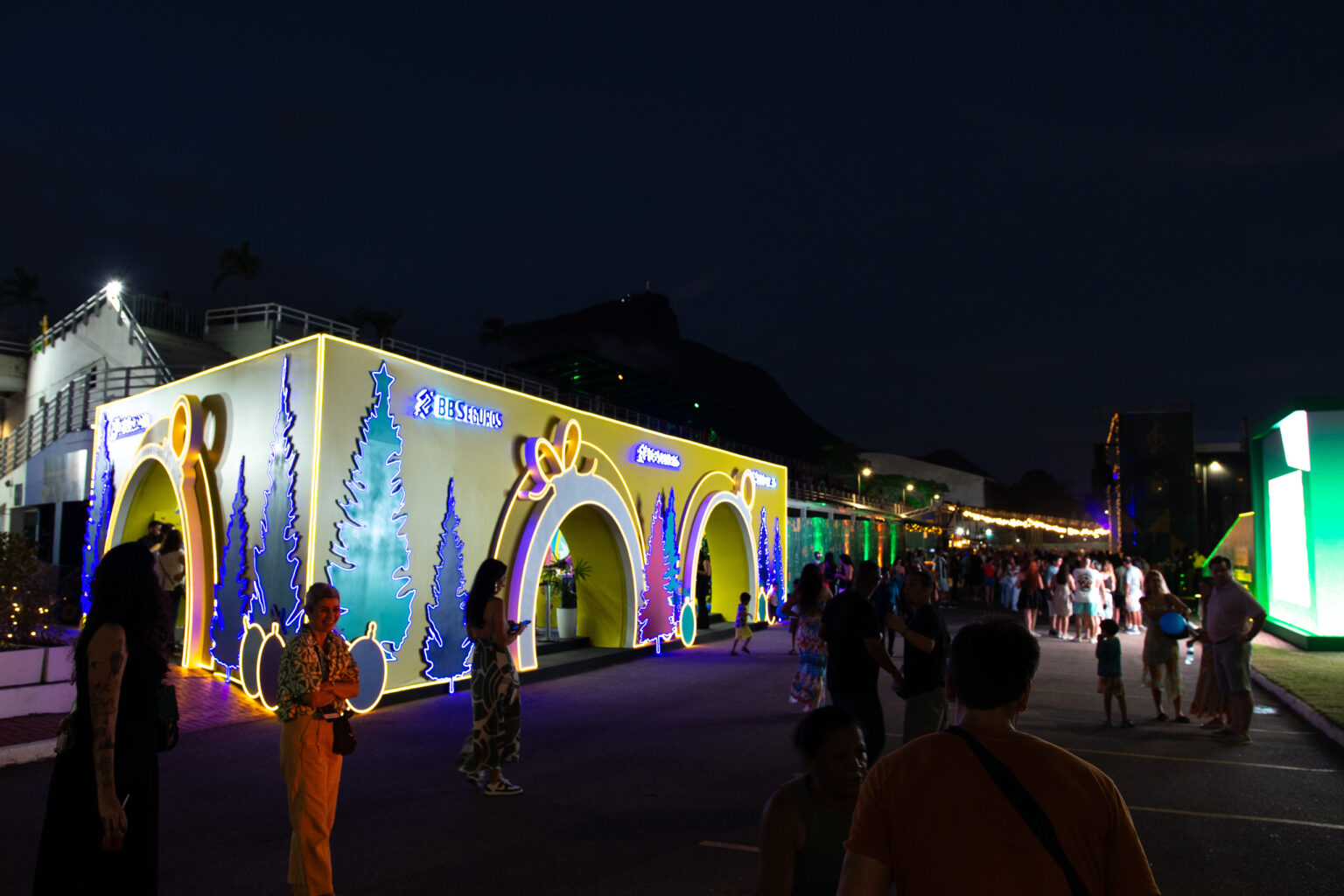 Ativação noturna da BB Seguros na Árvore do Rio, um estande iluminado em amarelo com arcos e desenhos temáticos de Natal.