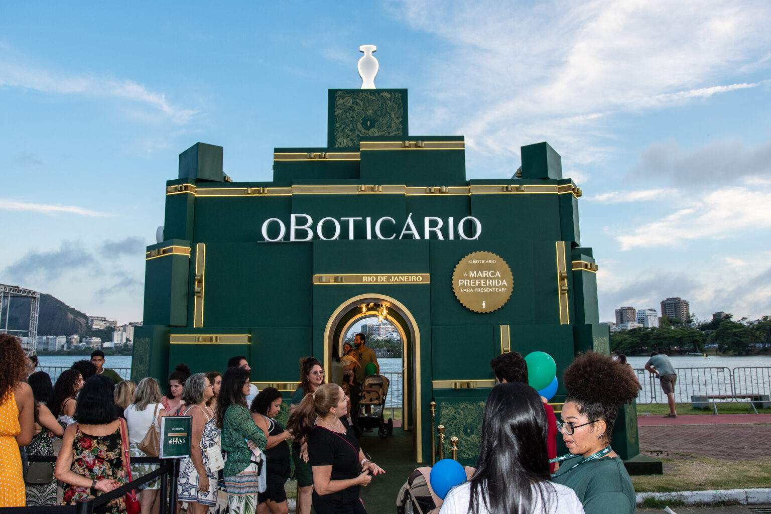 Ativação de O Boticário na Árvore do Rio, um estande verde escuro com a marca em destaque e pessoas na fila.