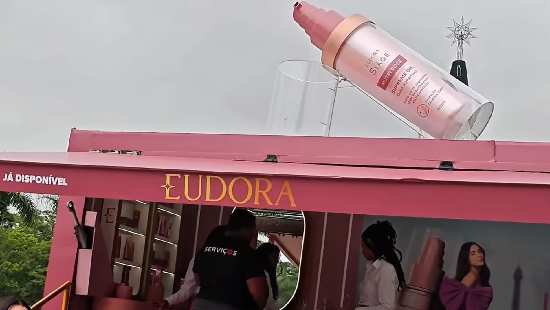 Unidade móvel rosa da marca Eudora com um frasco gigante do óleo capilar Siàge Nutri Rosé inclinado no teto, simulando a aplicação do produto.