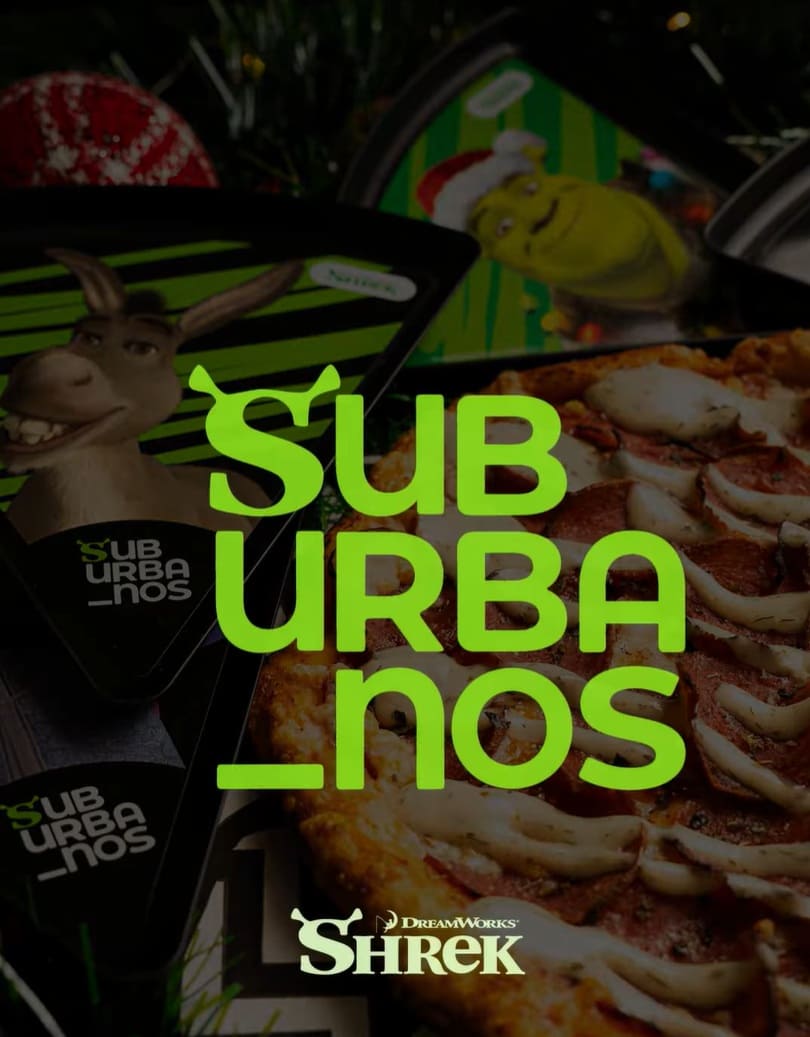 Imagem promocional da pizzaria Suburbanos com o logo em destaque sobre uma pizza, pratos colecionáveis do Shrek e o logo DreamWorks Shrek.