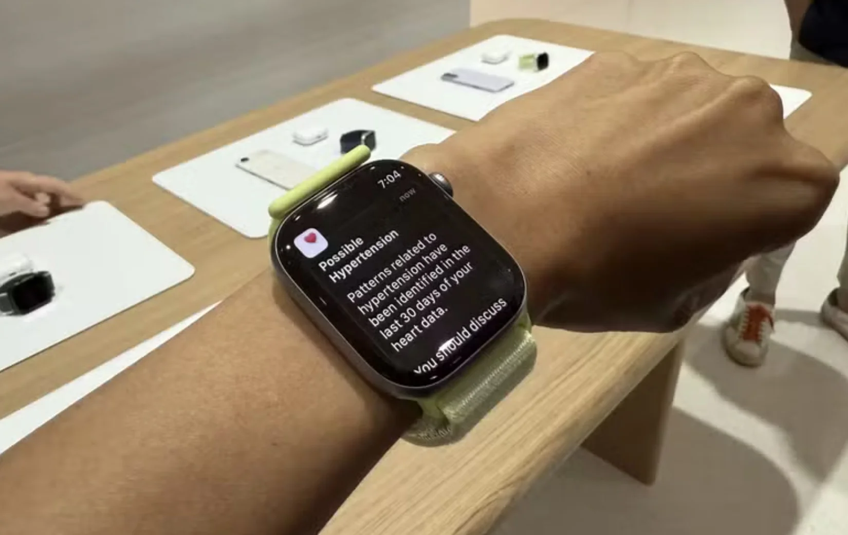 Close no pulso de uma pessoa usando um Apple Watch com pulseira verde clara. A tela exibe uma notificação de saúde intitulada "Possible Hypertension" (Possível Hipertensão), indicando que padrões relacionados à condição foram identificados nos últimos 30 dias.