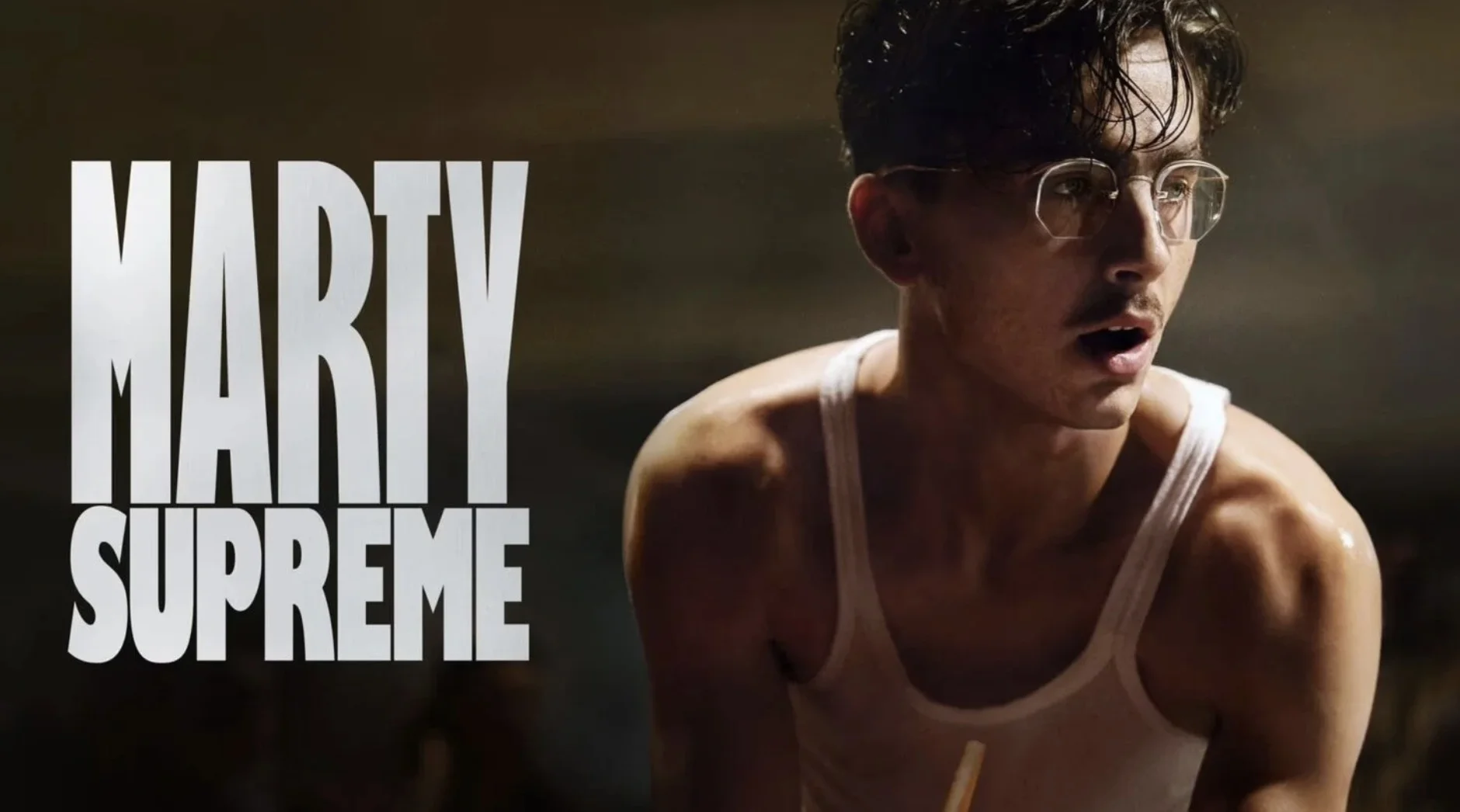 O ator Timothée Chalamet caracterizado para o filme 'Marty Supreme'. Ele usa óculos redondos e uma regata branca, com uma expressão concentrada. À esquerda, o título do filme está escrito em letras grandes e brancas.