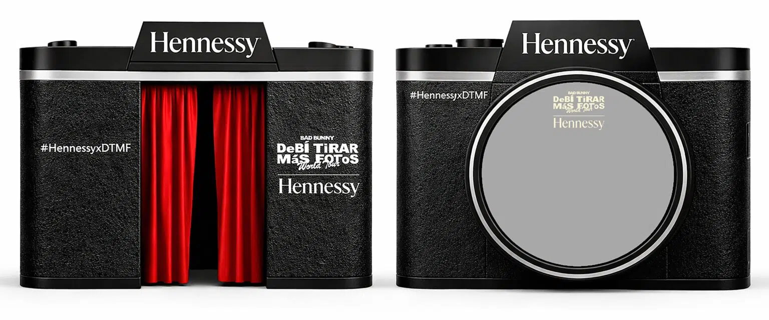 Uma estrutura 3D em formato de câmera fotográfica vintage preta com a marca Hennessy. No lugar da lente, há uma abertura com cortinas vermelhas, simulando uma cabine de fotos.