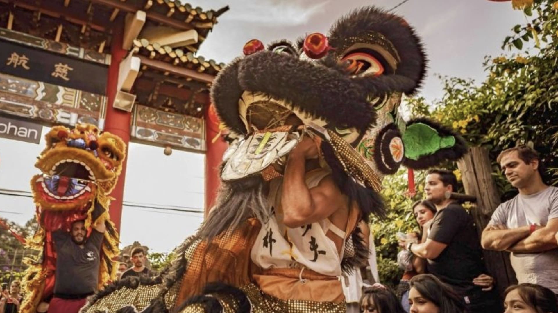Pessoas realizam a Dança do Leão durante a celebração do Ano Novo Chinês na Liberdade, em São Paulo, diante de um portal tradicional e do público.