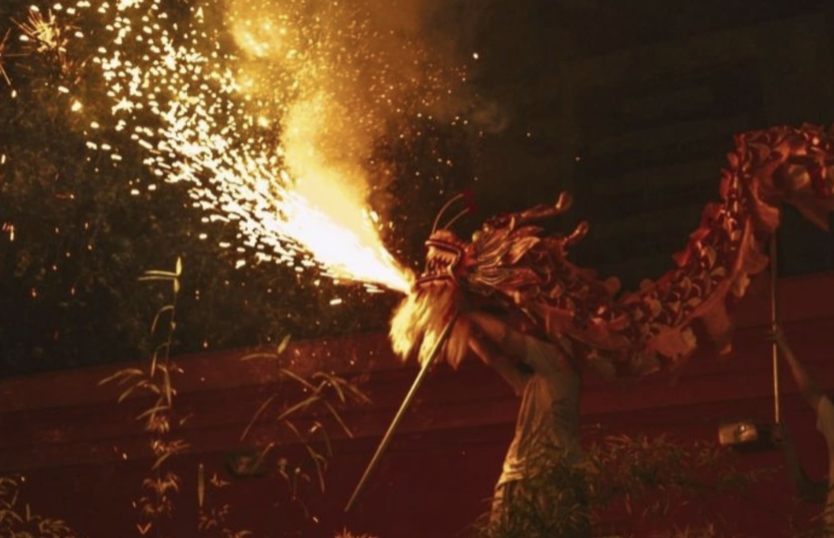 Integrantes de um grupo de dança performam a Dança do Leão em frente a um portal tradicional chinês na Liberdade, em São Paulo, enquanto o público observa.