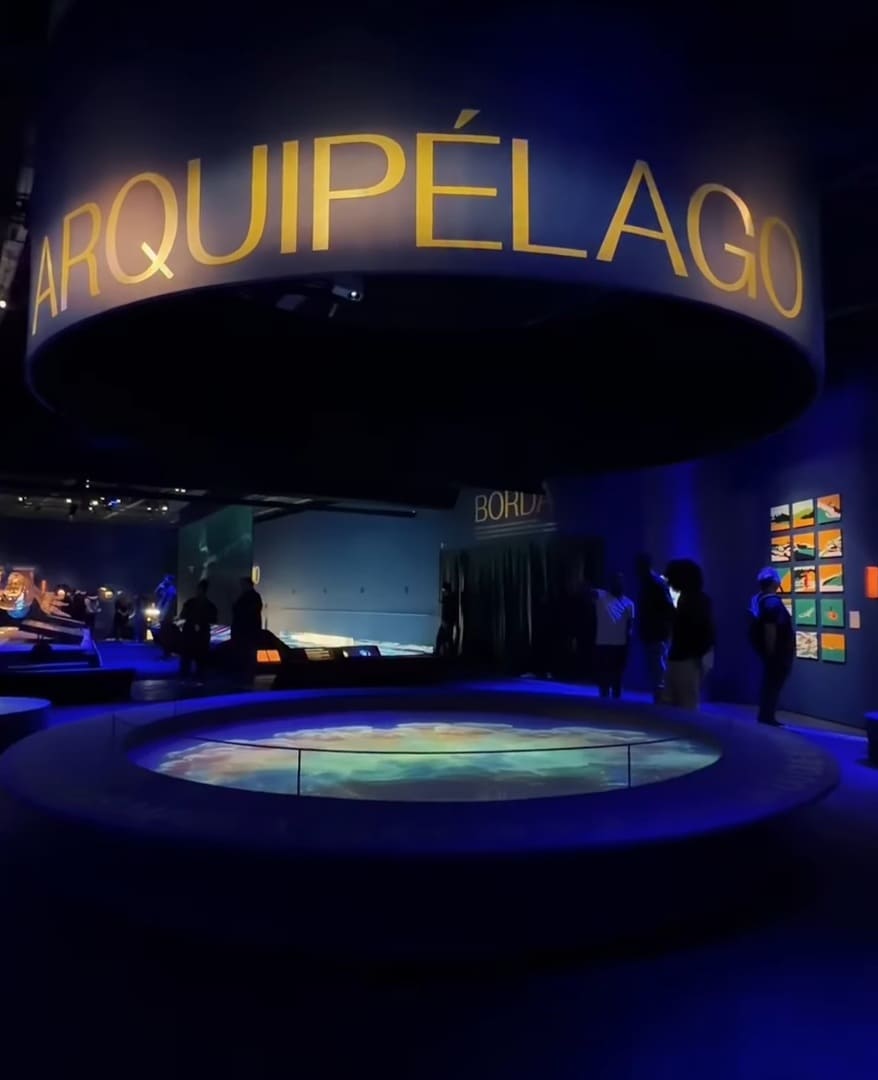 Galeria de museu com paredes azuis, quadros emoldurados e uma grande estrela branca de oito pontas iluminada na parede.