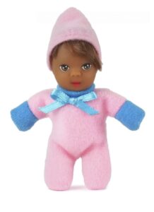 Boneca pequena de pele negra vestindo macacão e gorro de feltro rosa, com detalhes em azul e um laço de fita azul no pescoço.