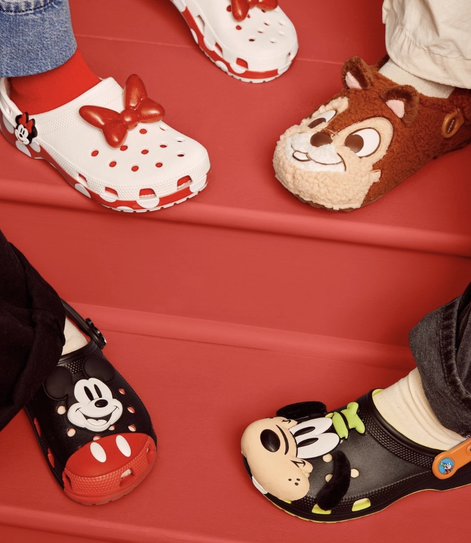 Quatro pessoas usando diferentes modelos da coleção Disney x Crocs em uma escada vermelha.