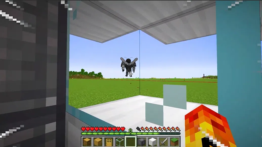 Captura de tela do Minecraft mostrando um mosquito gigante através de uma janela de vidro. Descrição curta: Visão em primeira pessoa dentro de uma construção no Minecraft. Através do vidro, observa-se um mosquito Aedes aegypti estilizado voando sobre um campo verde. O jogador segura um item que emite chamas.