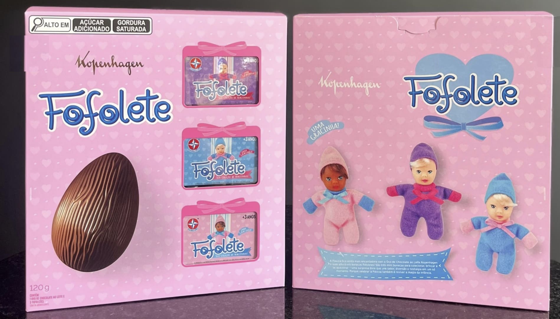 Frente e verso da caixa rosa do Ovo de Páscoa Kopenhagen Fofolete. A embalagem de 120g possui selos de "alto em açúcar adicionado e gordura saturada". A frente mostra o ovo de chocolate e janelas com três mini Fofoletes em suas caixinhas originais (rosa, azul e roxa); o verso exibe as três bonecas fora da caixa com a frase "Uma gracinha!".