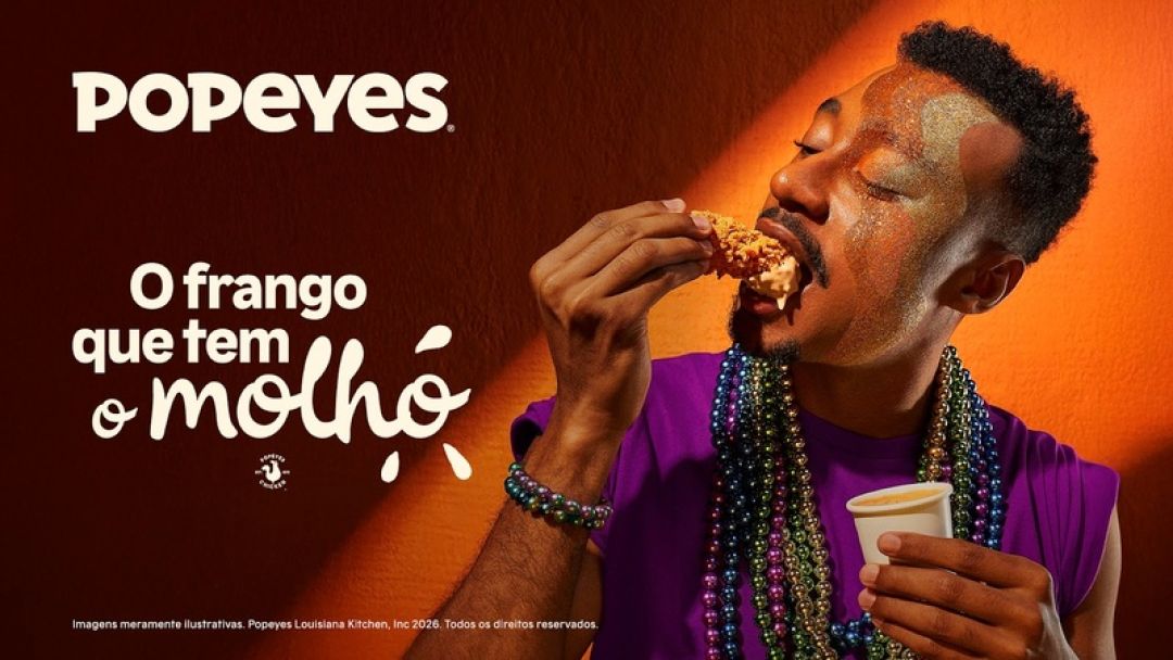 Propaganda da Popeyes com um homem negro usando colares coloridos e glitter no rosto, mergulhando um pedaço de frango frito em um pote de molho. O fundo é laranja vibrante com o texto 'O frango que tem o molho'.