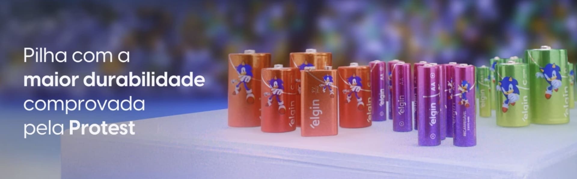Banner publicitário horizontal com diversas pilhas coloridas da Elgin estampadas com o personagem Sonic. À esquerda, o texto: "Pilha com a maior durabilidade comprovada pela Protest".