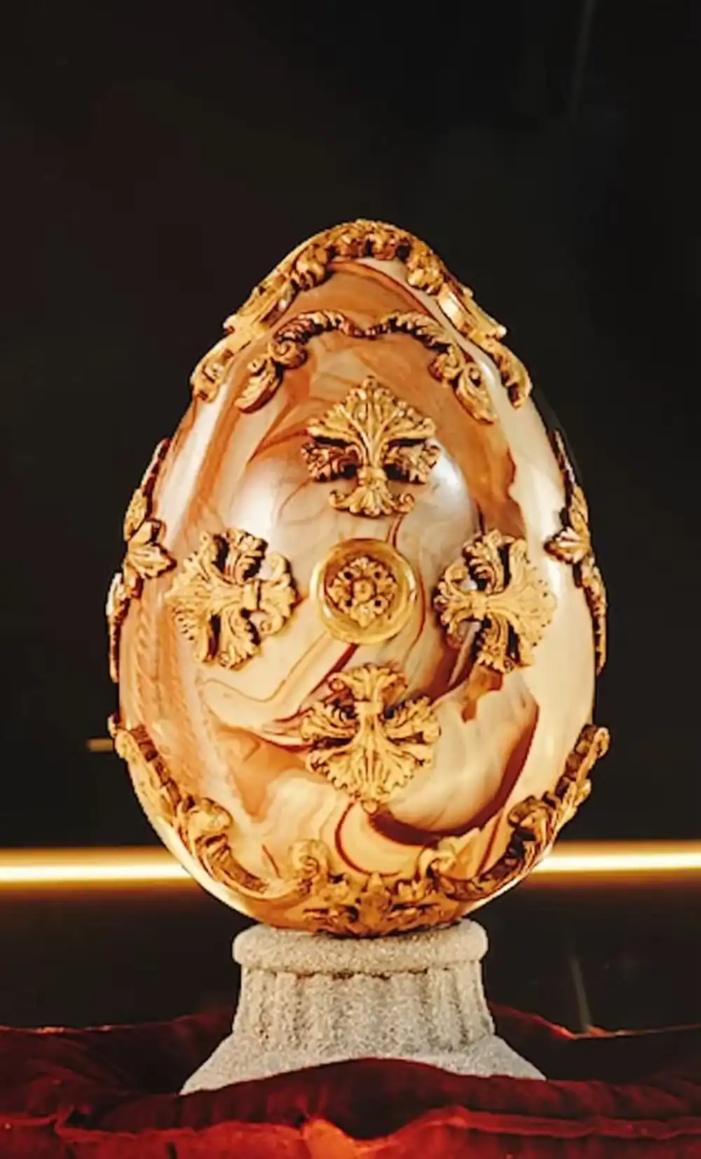 Um close de um ovo decorativo de mármore marrom e preto em um pedestal de pedra com detalhes dourados.