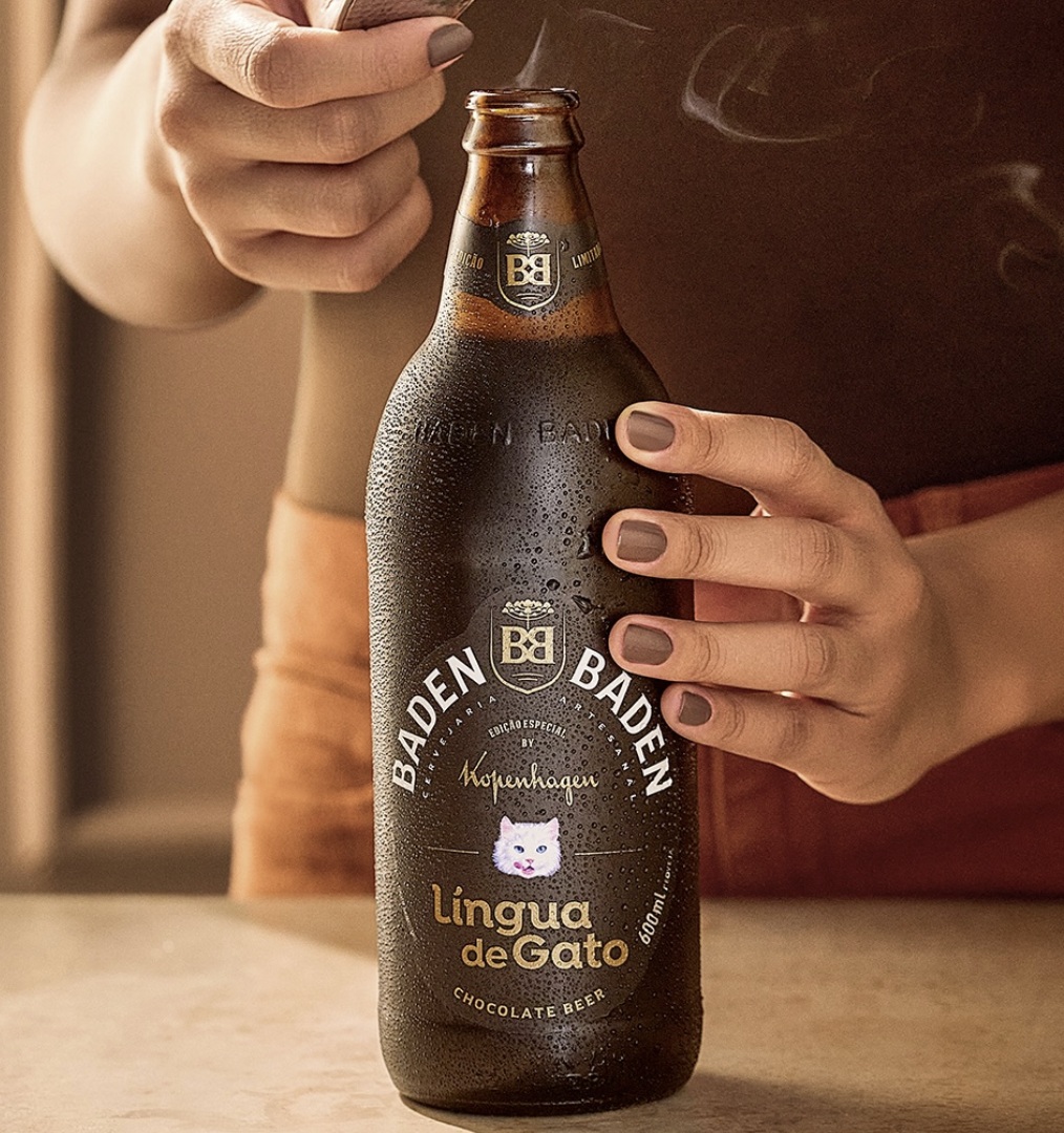 Close em uma mão segurando uma garrafa de 600ml da cerveja Baden Baden Língua de Gato, que está gelada e com gotículas de condensação.