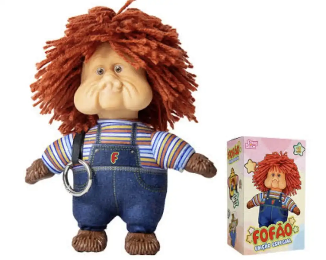 Miniatura do boneco Fofão com argola de chaveiro presa ao ombro, ao lado de sua embalagem temática decorada com estrelas.