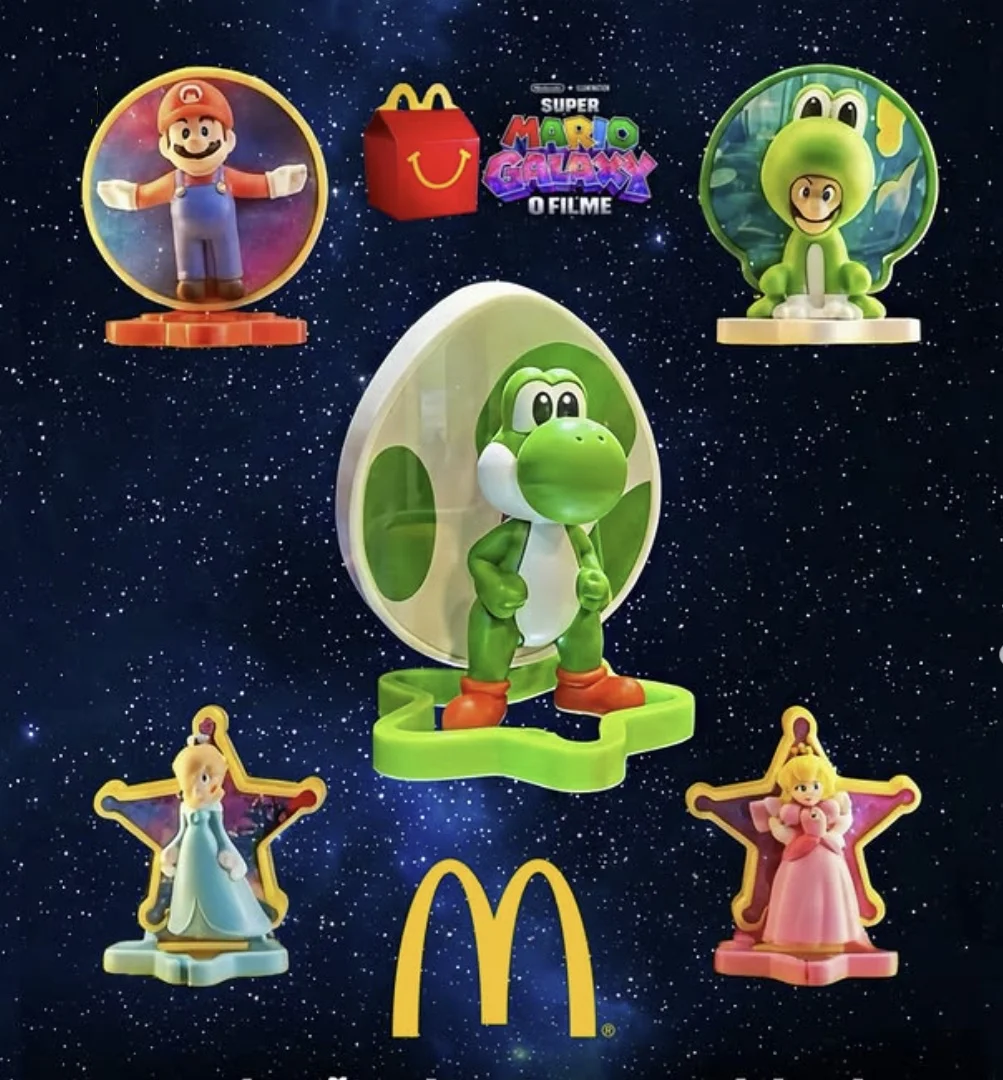 Cinco miniaturas 3D da coleção Super Mario Galaxy sobre um fundo de espaço estrelado. Inclui Mario, Luigi com roupa de sapo, Yoshi em um ovo gigante, Princesa Rosalina e Princesa Peach, com os logotipos do McDonald's e do filme ao centro.