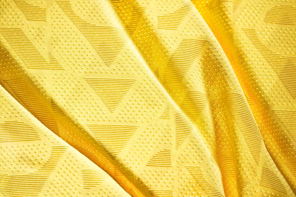 close-up de tecido de jérsei de futebol amarelo texturizado com padrão geométrico em relevo.