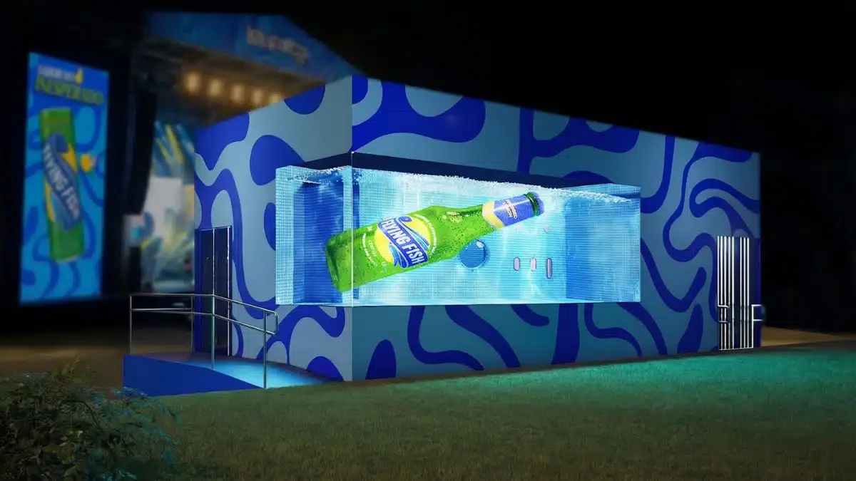Ativação da marca Flying Fish no festival Lollapalooza: um estande cúbico azul com padrões abstratos e um grande painel digital 3D que simula uma garrafa de cerveja mergulhada em água borbulhante.