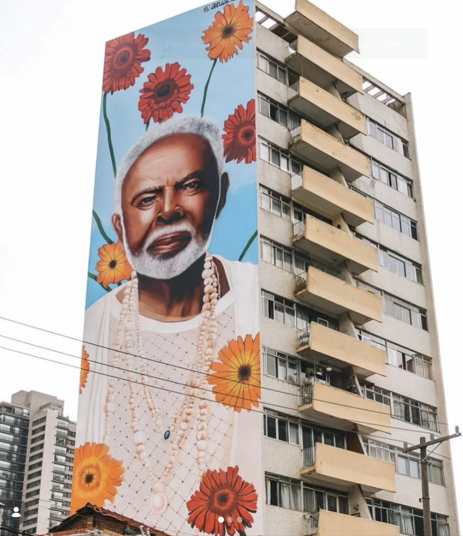 Mural artístico de Gilberto Gil em um prédio residencial, visto de um ângulo inferior na rua.